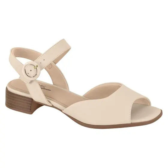 Product shot of a cream-colored low block heel sandal with an ankle strap and gold buckle featuring a slightly squared toe and a wooden heel