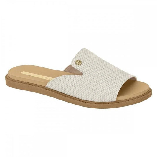 Product shot of a beige  slide sandal featuring a textured upper a gold accent and a light brown sole
