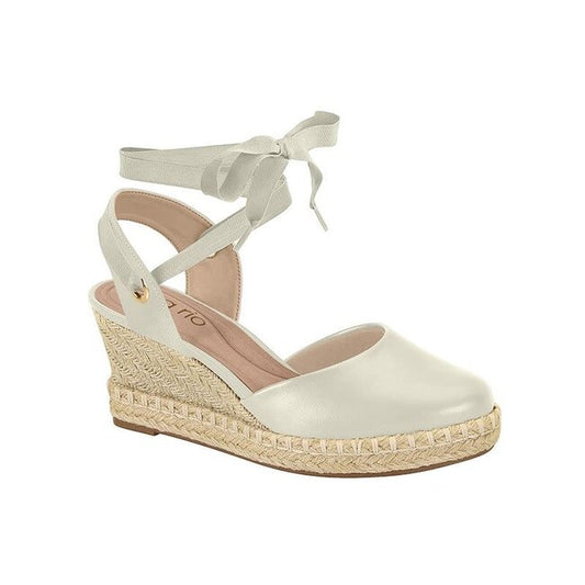 Product shot of a beige espadrille wedge sandal with a delicate ribbon tie featuring a woven jute platform and a subtle gold accent