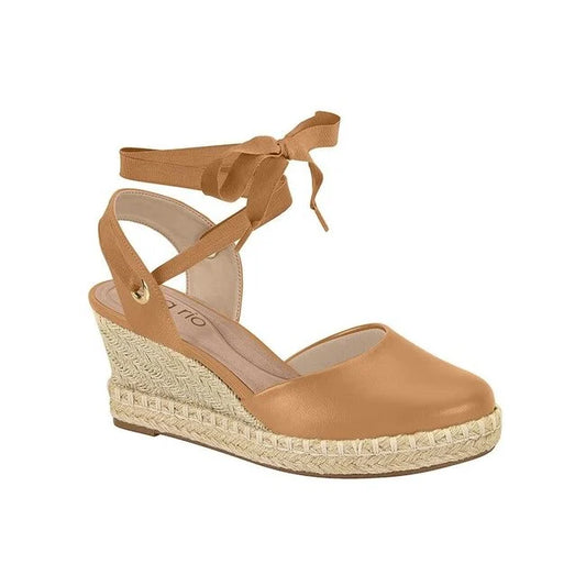 Product shot of a tan espadrille wedge sandal with a ribbon tie featuring a woven jute platform and a gold detail
