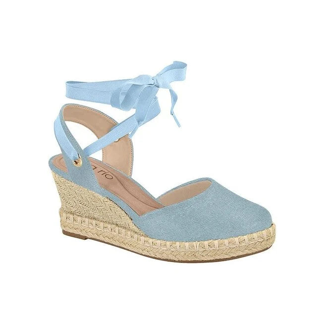 Product shot of a light blue denim espadrille wedge sandal with a matching ribbon tie and gold accents on the jute platform sole
