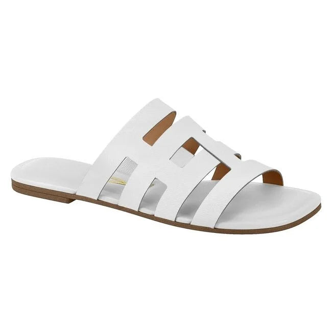 Product shot of a white leather slide sandal with cutout details featuring a brown sole and subtly embossed branding
